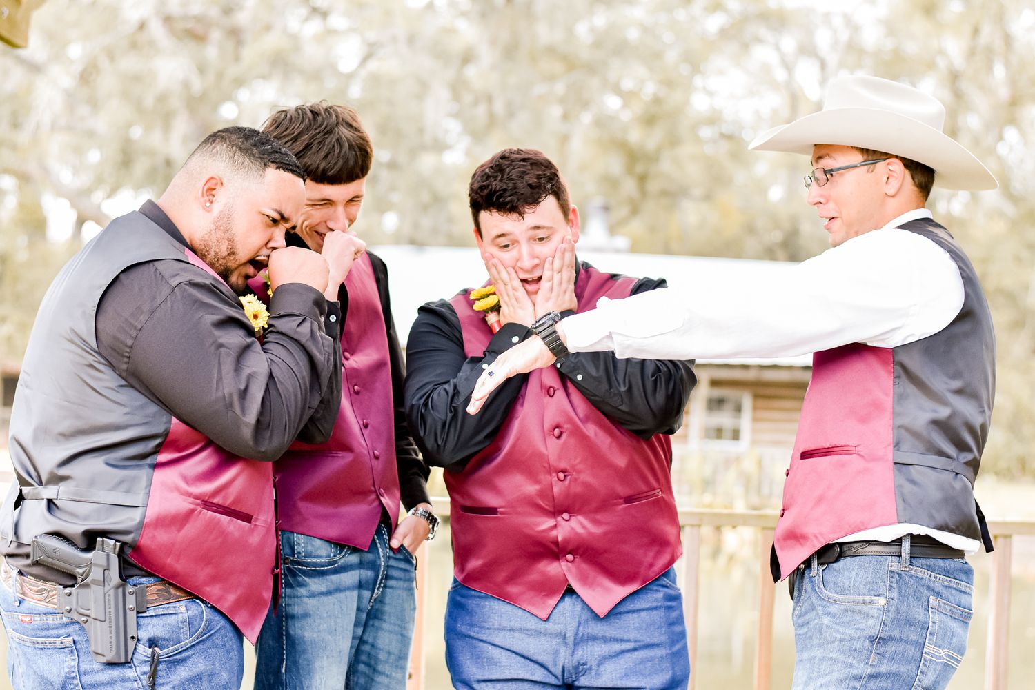 Groomsmen in burgundy vests sharing laughs during outdoor wedding celebration.