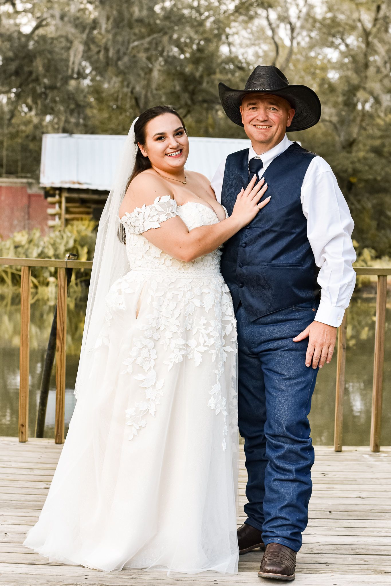 Wedding couple poses on wooden dock with rustic barn in background.