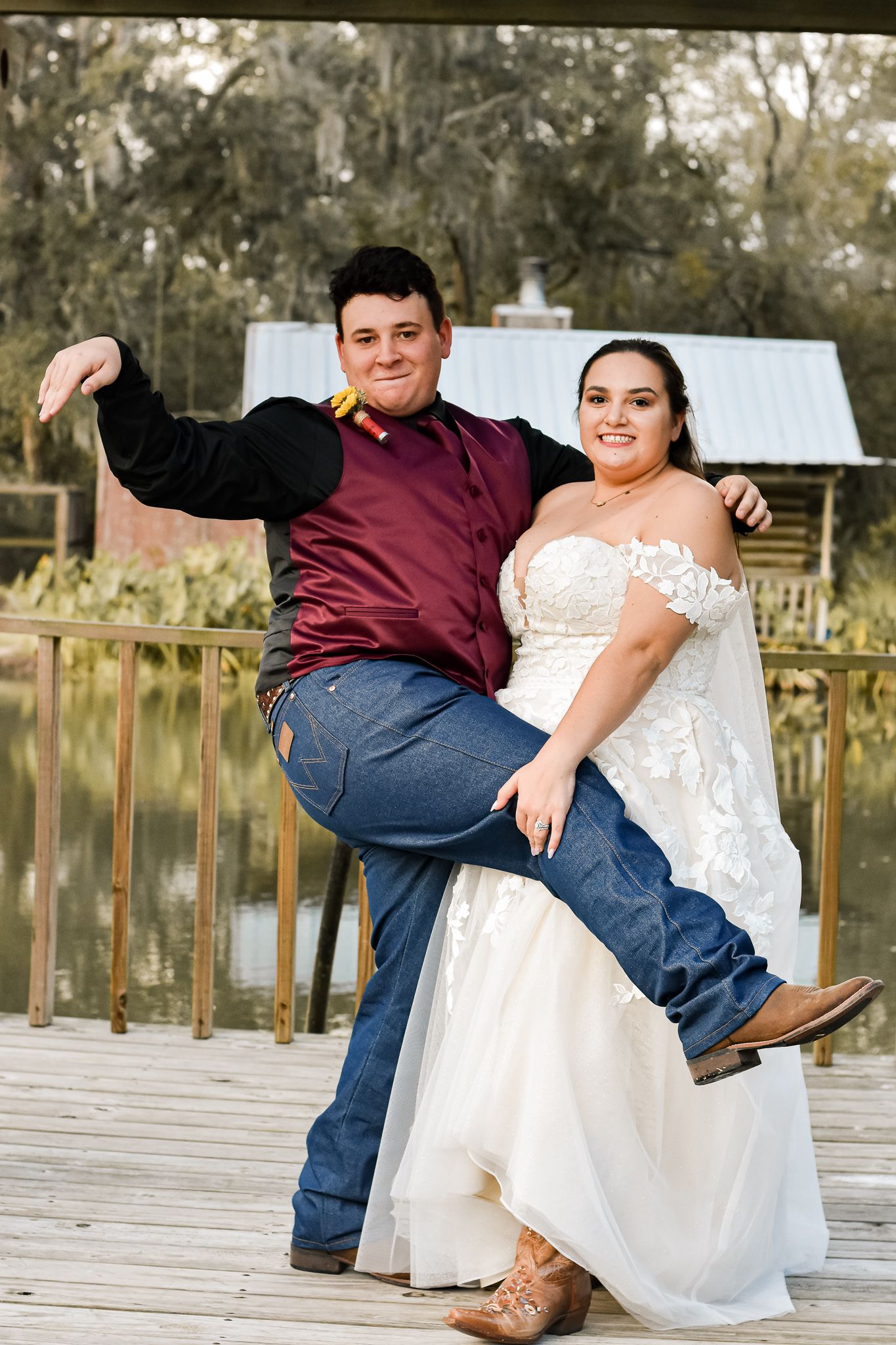 A couple strikes a playful pose on a wooden deck with a rustic cabin in the background.