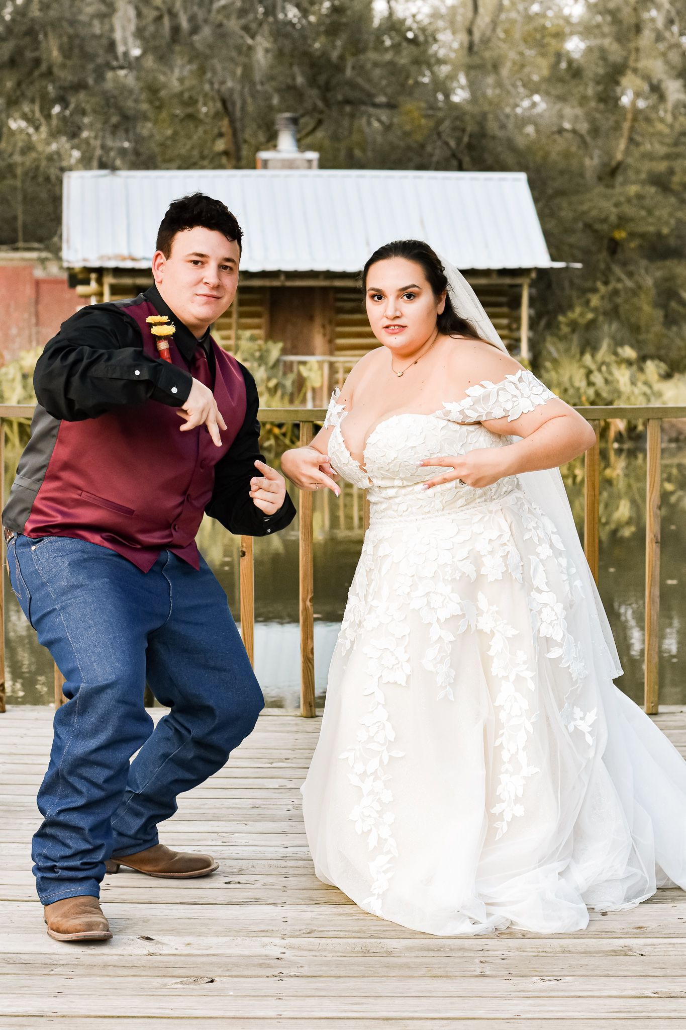 A couple poses together in wedding attire on a rustic wooden deck during their special day.