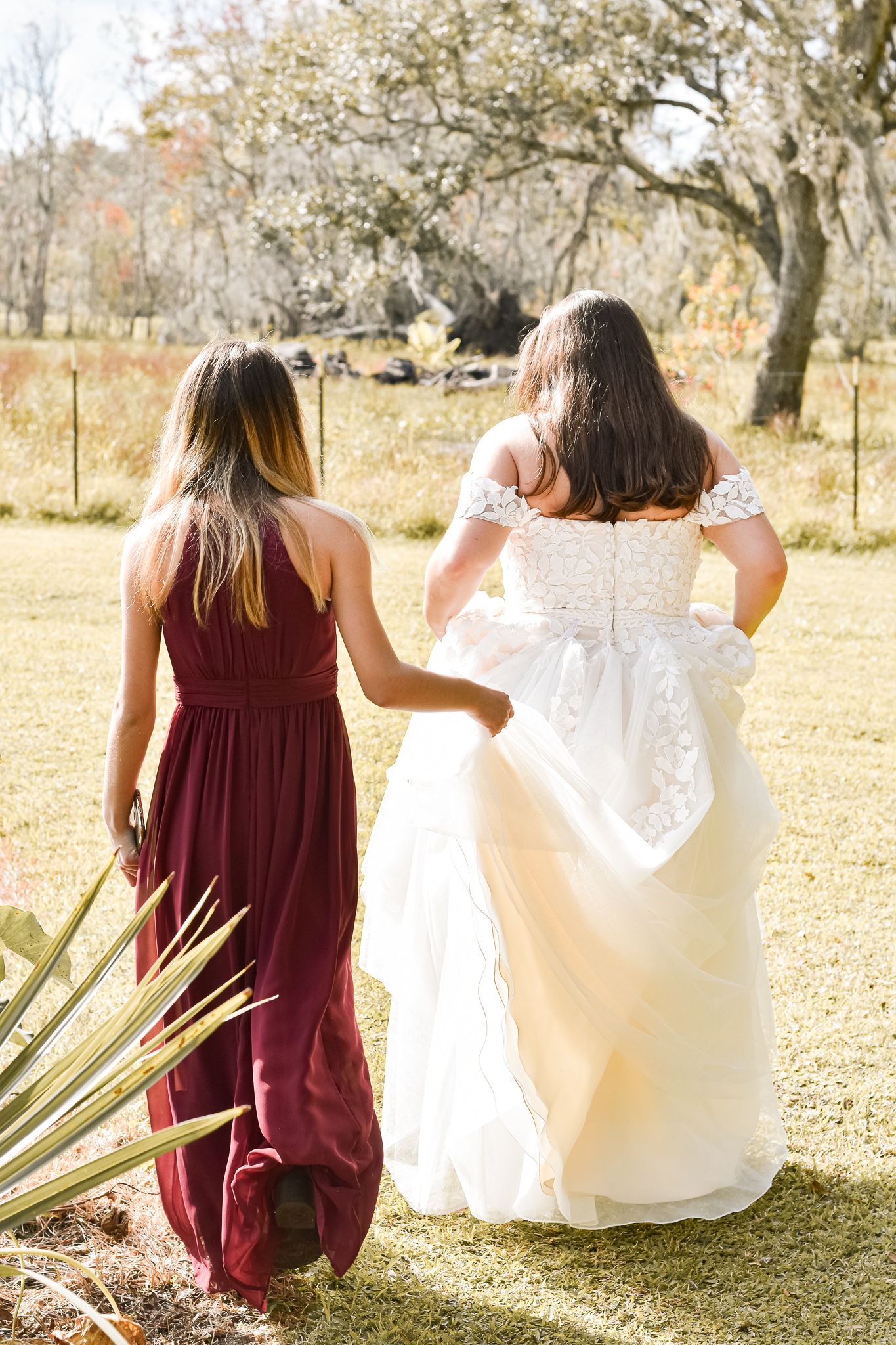 Two women in burgundy and white dresses walking together in a sunlit outdoor setting.