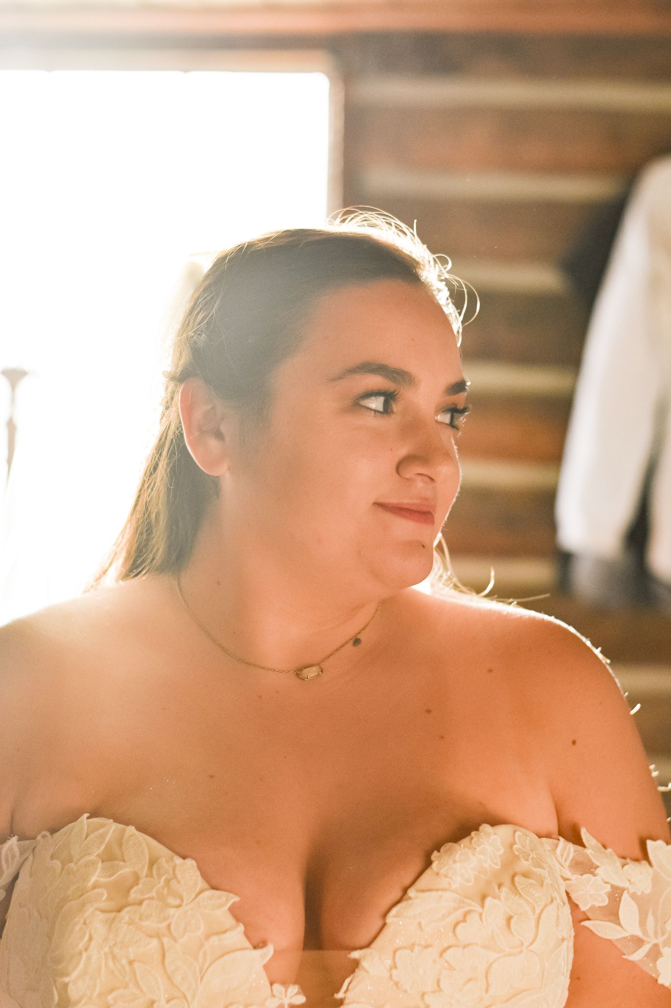 A bride in an off-shoulder lace wedding dress poses in warm sunlit room.