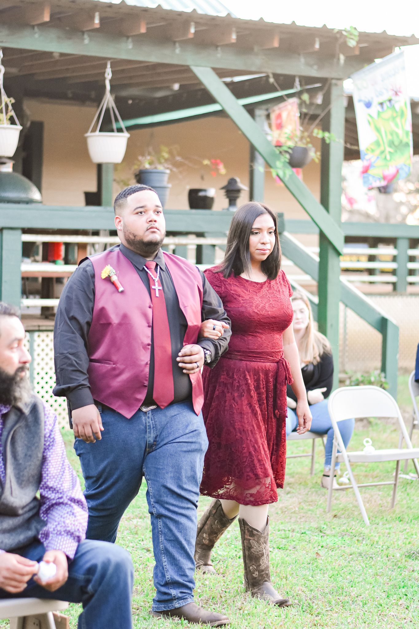 Guests in burgundy formal attire walking at an outdoor wedding venue.
