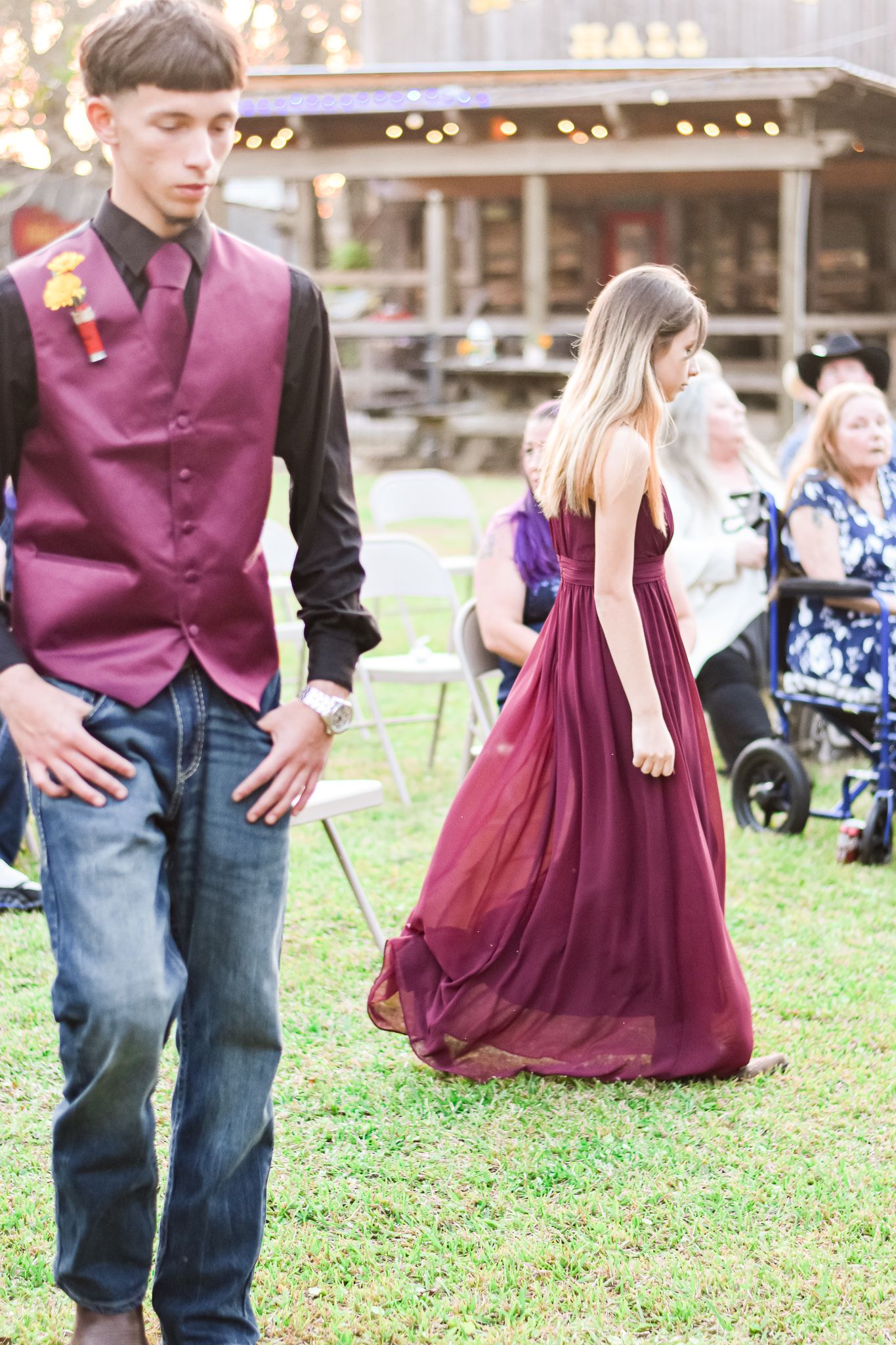 Wedding guests in burgundy attire standing on grass at an outdoor reception.