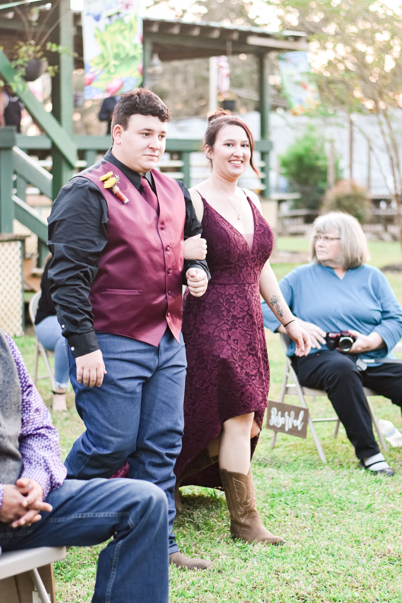 Wedding guests in burgundy attire mingle at an outdoor reception.