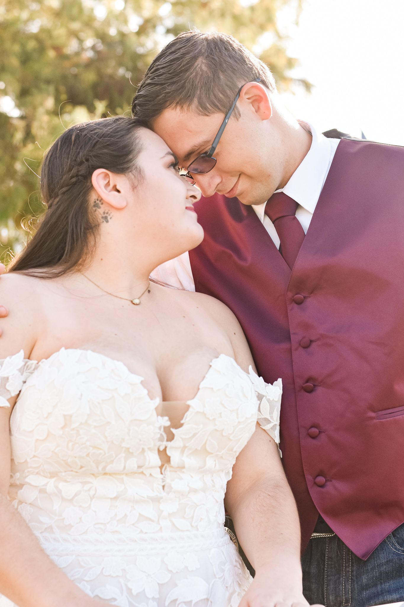 An intimate moment between a couple in burgundy and white wedding attire during sunset.