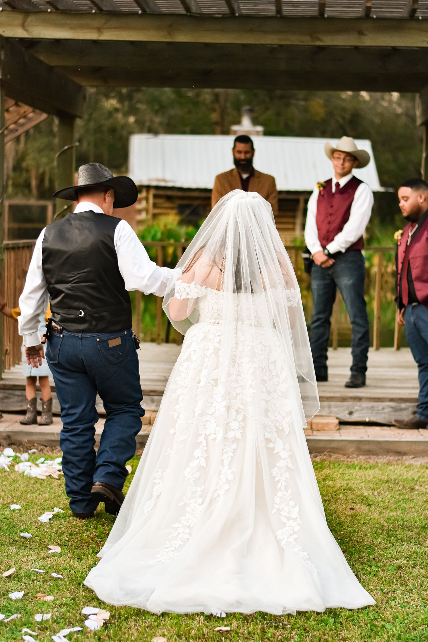 Wedding ceremony on rustic wooden deck with bride in flowing white veil and gown.