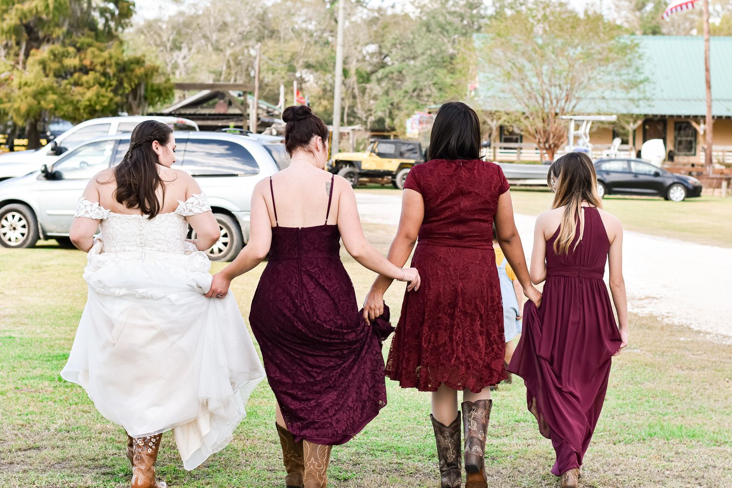 Bridesmaids in burgundy dresses walking together outdoors holding their dress skirts.