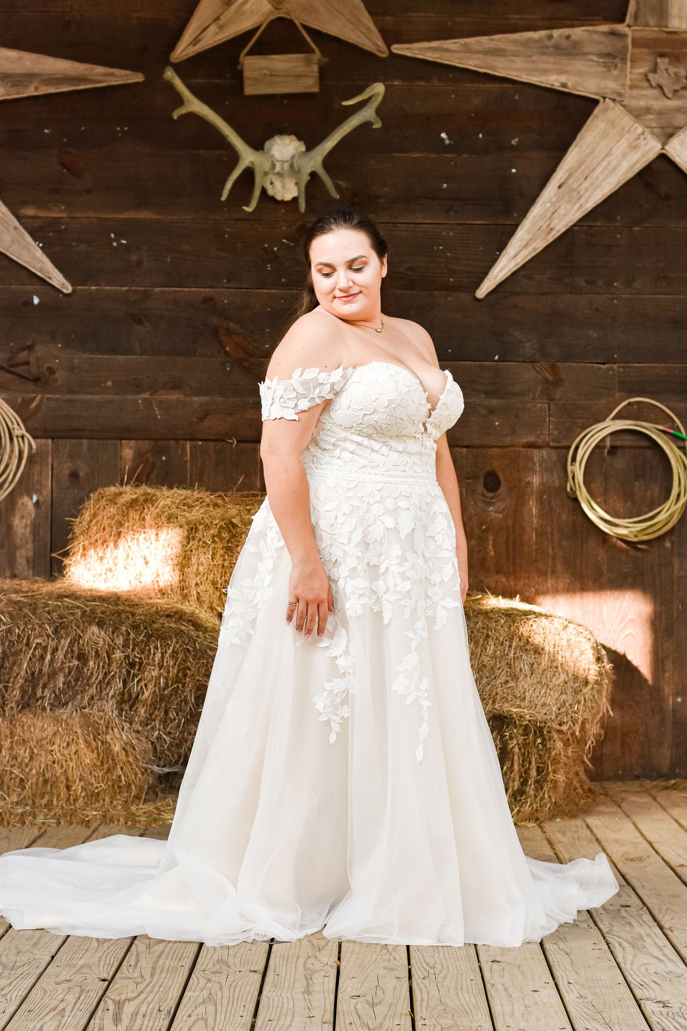 Elegant lace wedding gown displayed against rustic barn wall with decorative stars and hay bales.