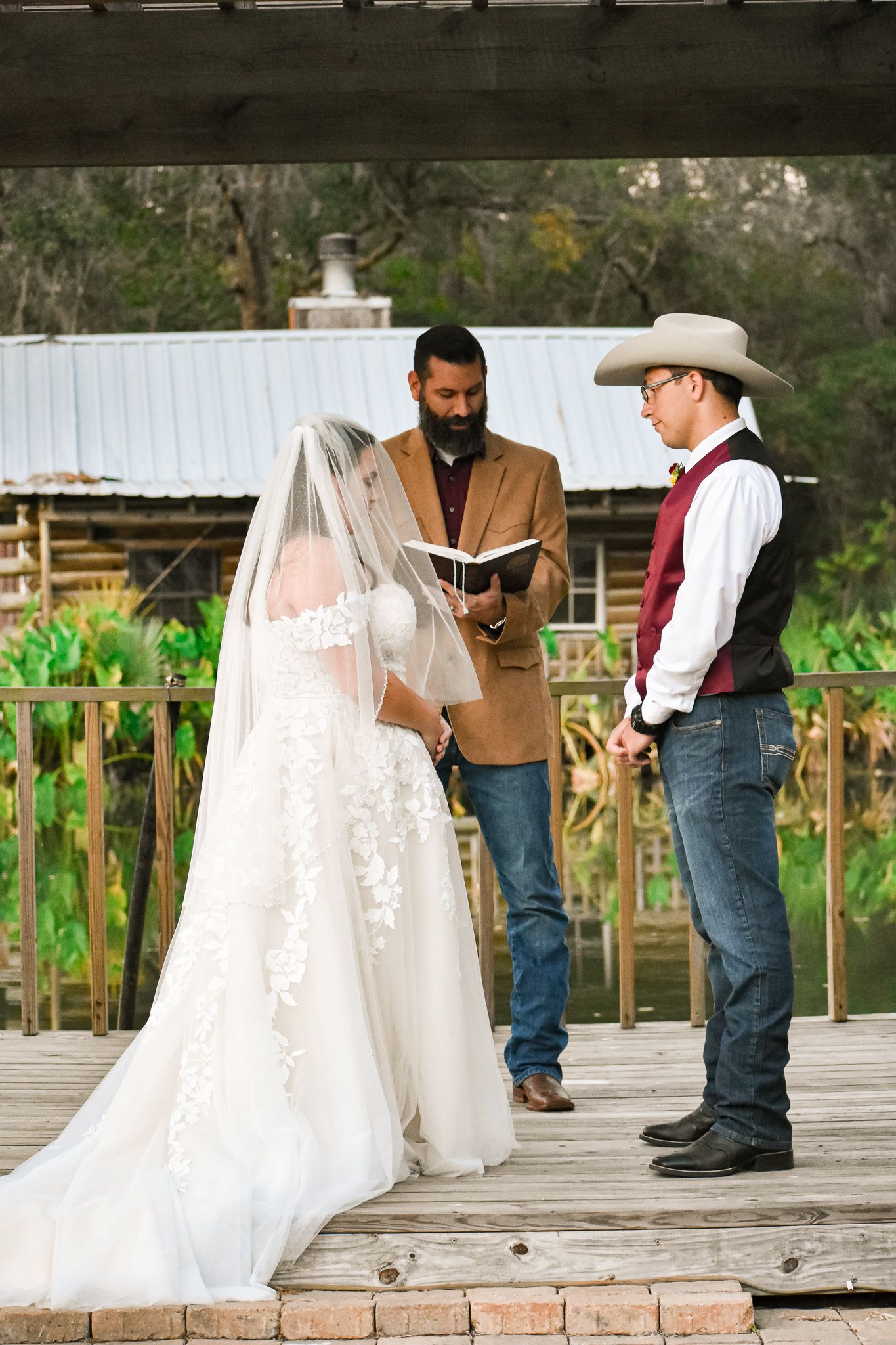 Outdoor wedding ceremony on wooden deck with officiant and couple in country western attire.