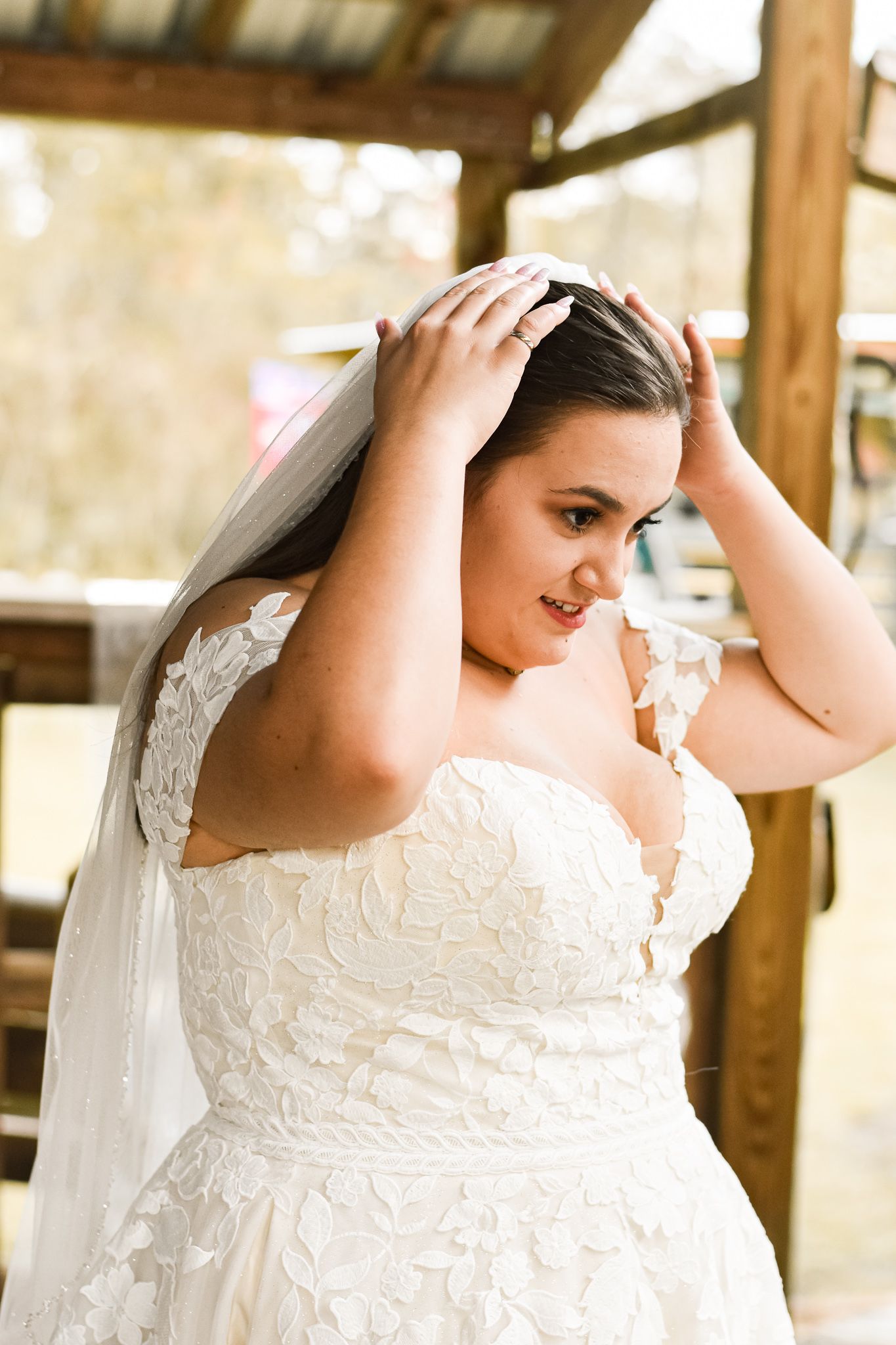 Candid moment of bride adjusting veil in rustic outdoor setting.