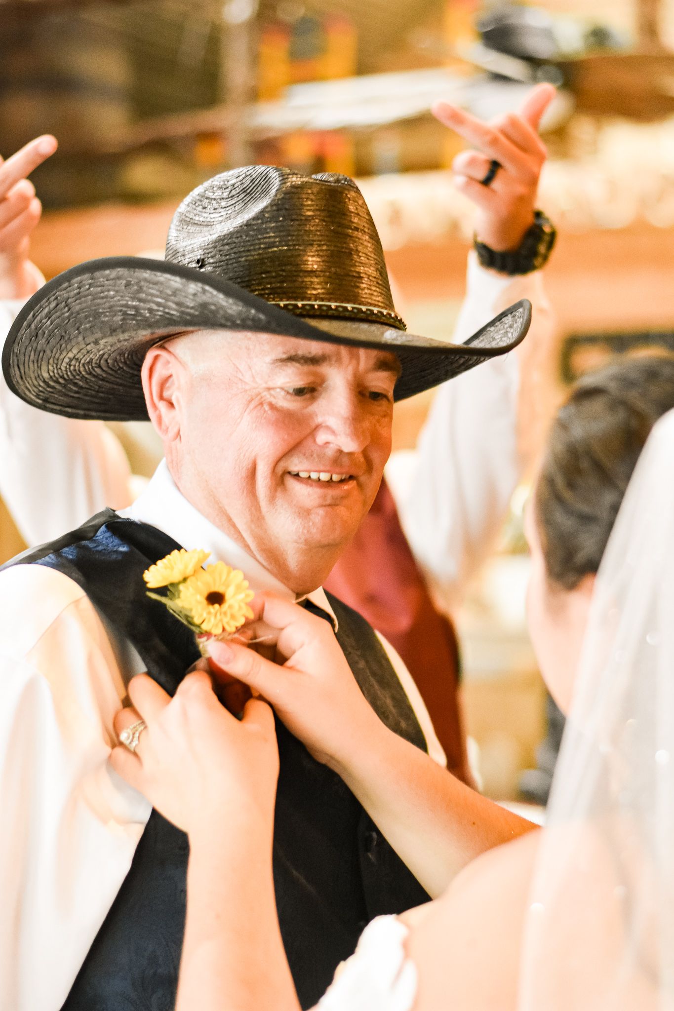 Joyful moment during western wedding as boutonniere is pinned on guest in cowboy hat.