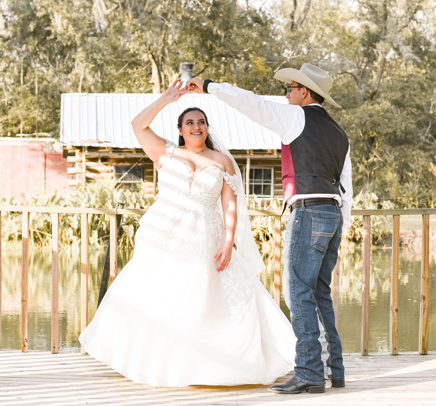 Couple dancing together on a wooden dock by a lake, with the bride in a white gown and groom in western attire.