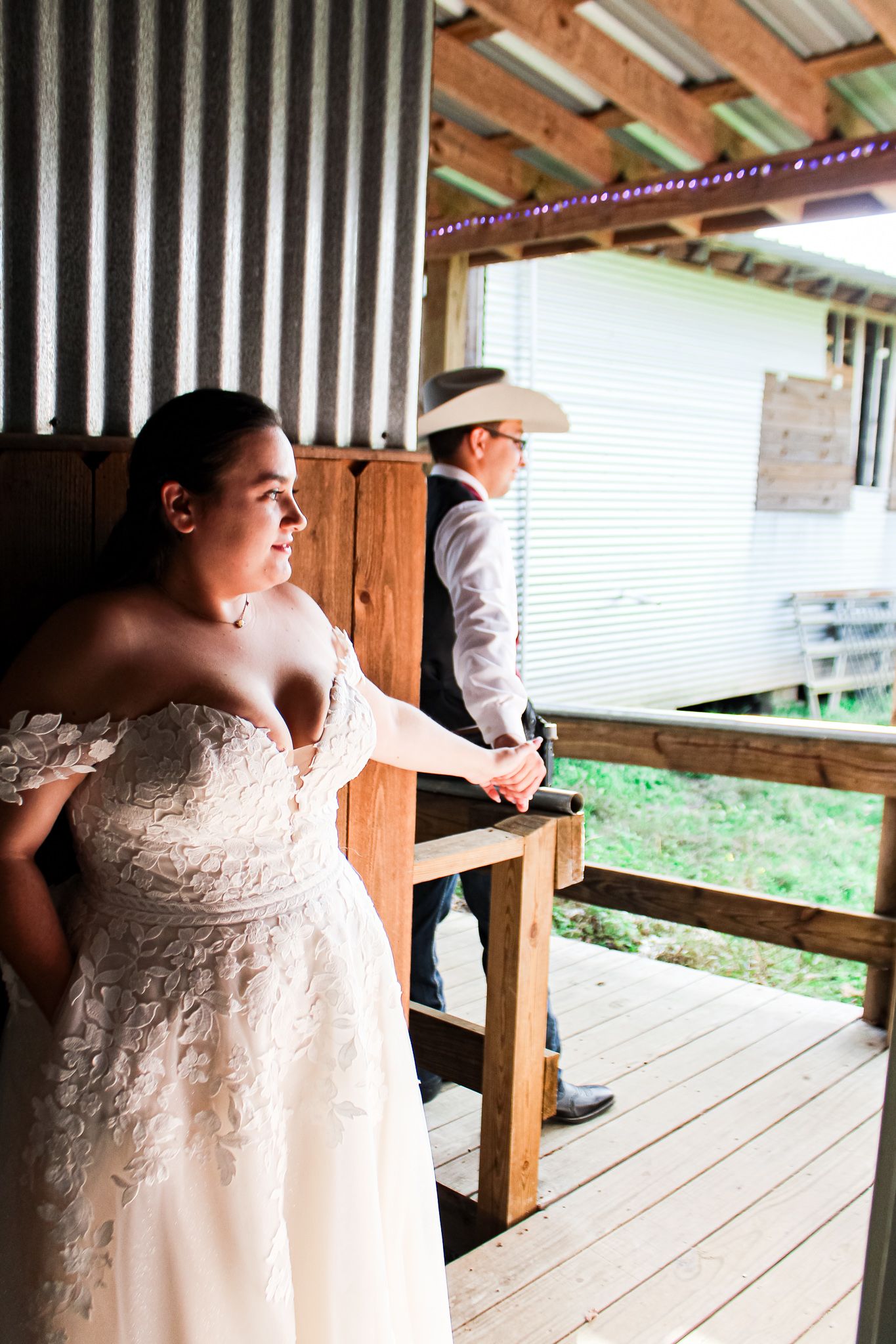 Bride in lace dress stands on rustic wooden porch during first look moment.