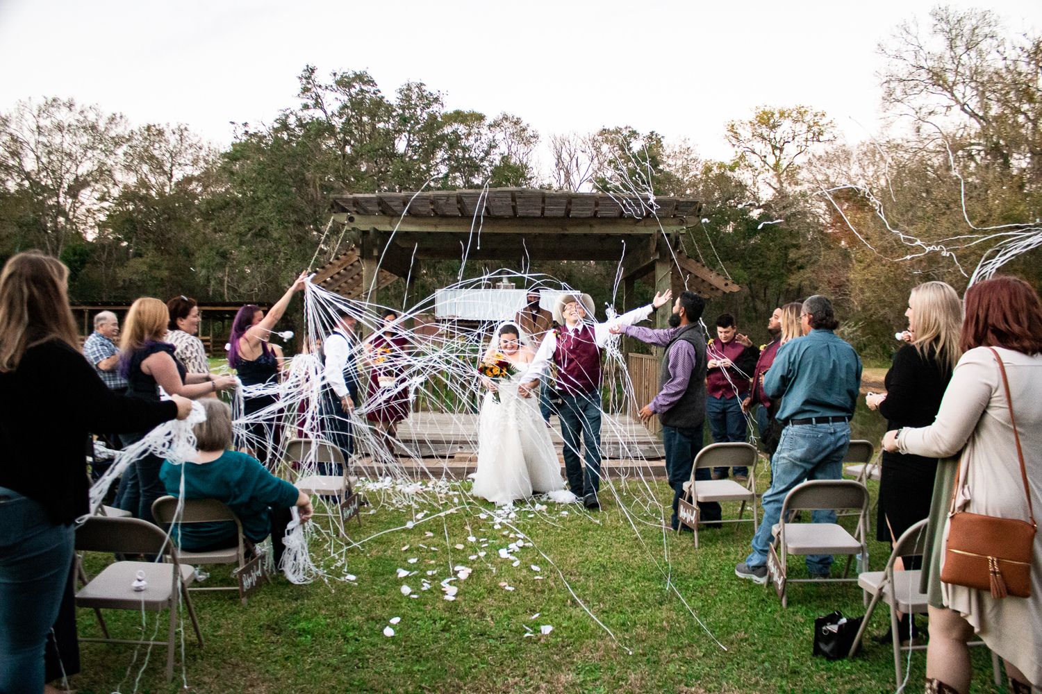 Wedding recessional with guests holding streamers as couple exits outdoor ceremony.