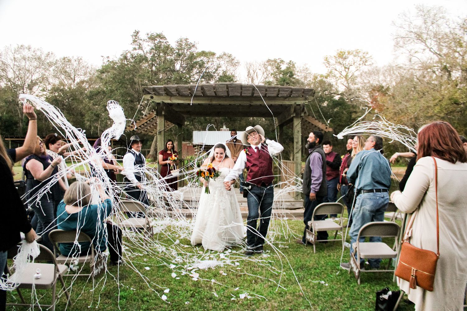 Wedding party walks through a shower of white streamers during outdoor ceremony celebration.