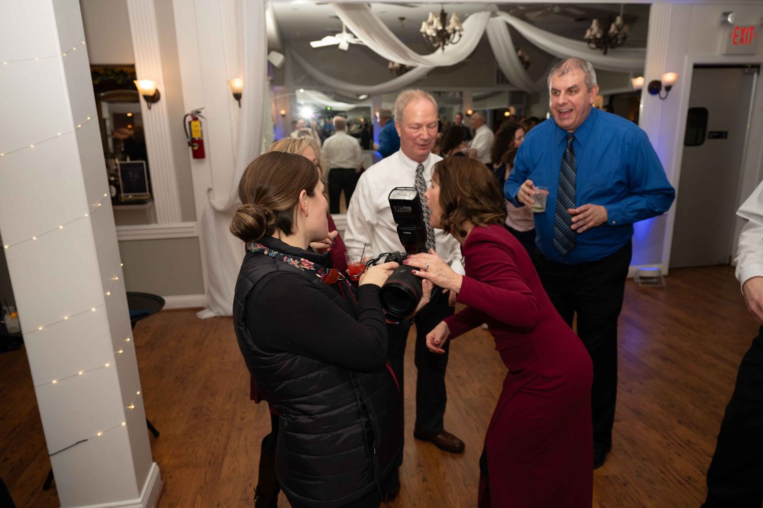 A group of guests mingling and socializing at an indoor event with white draped decorations.