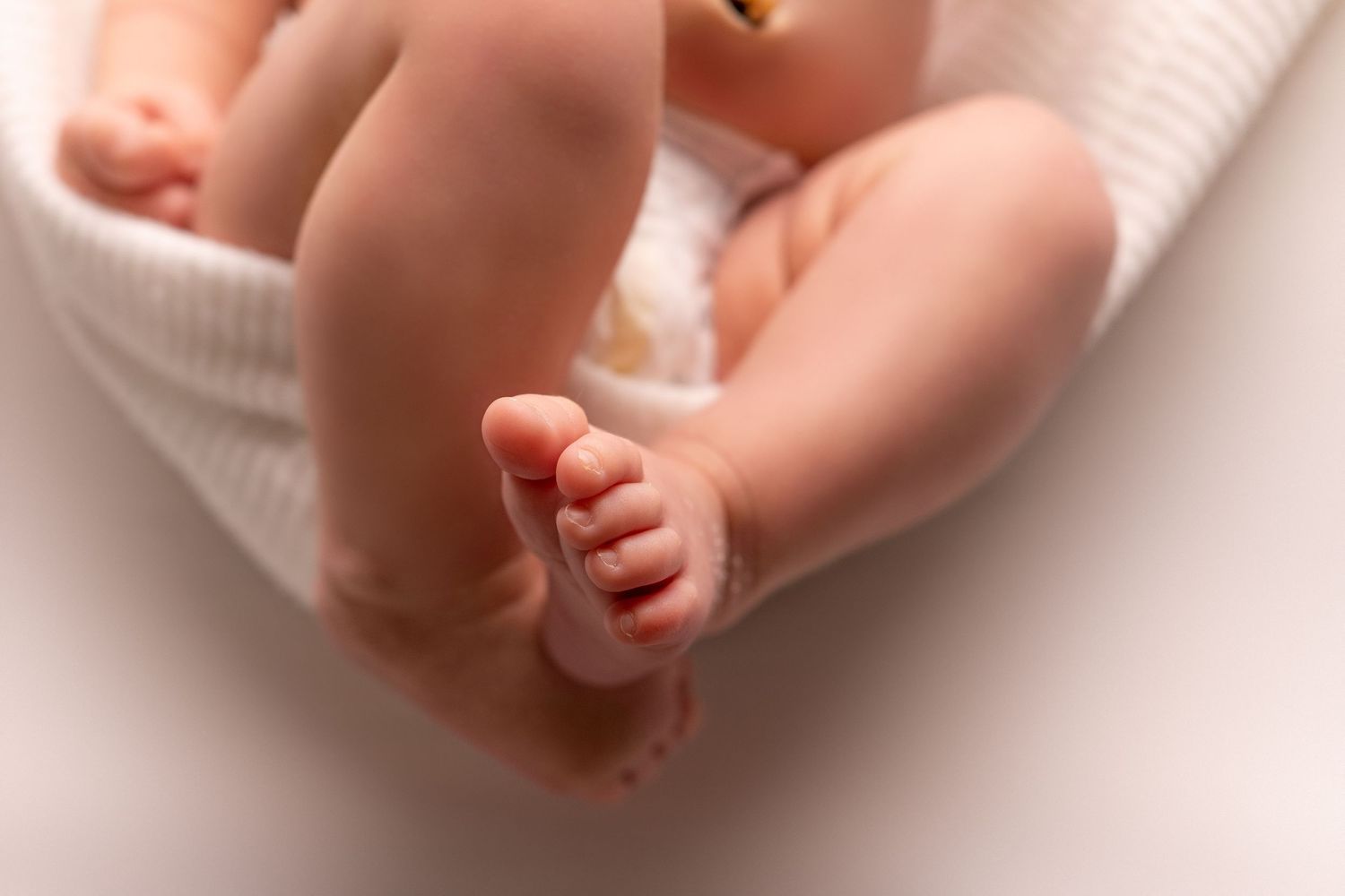 Close-up of tiny newborn feet and toes on white textured fabric.