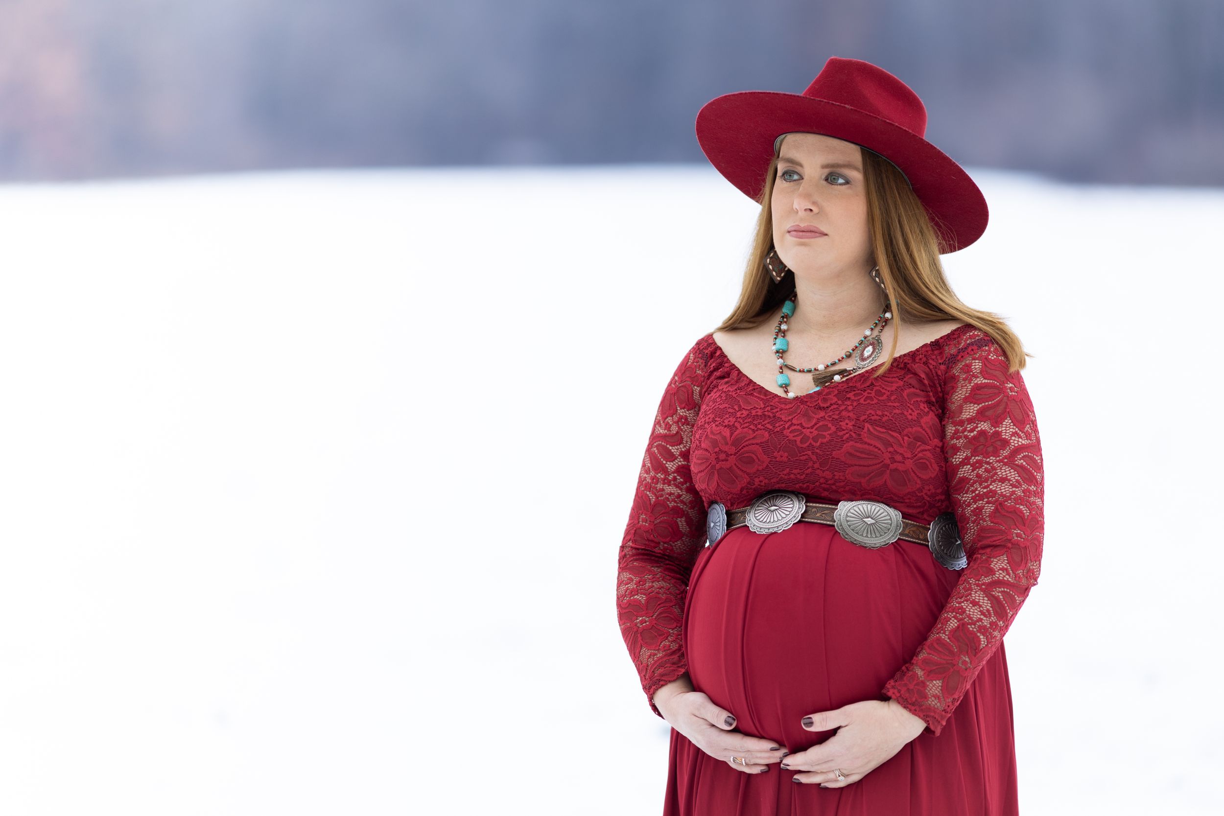 A pregnant cowgirl looking across the horizon of her snow-laden horse farm.