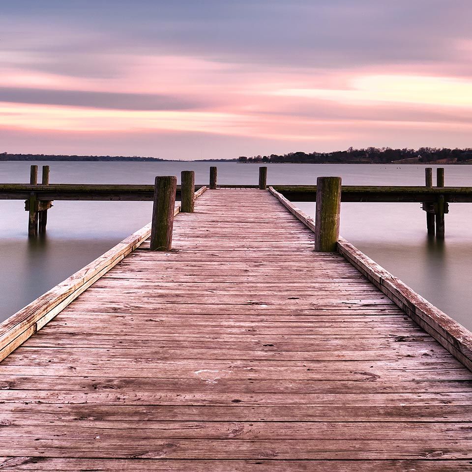 Wooden pier extending into calm waters during a pink and purple sunset.