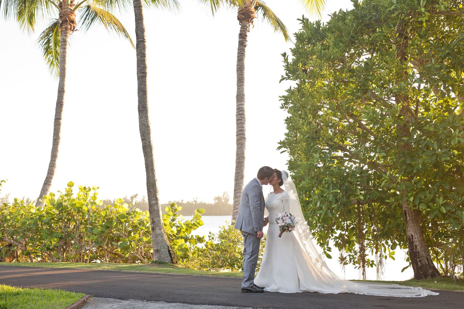 Beach wedding ceremony setup with palm trees and ocean view at sunset.