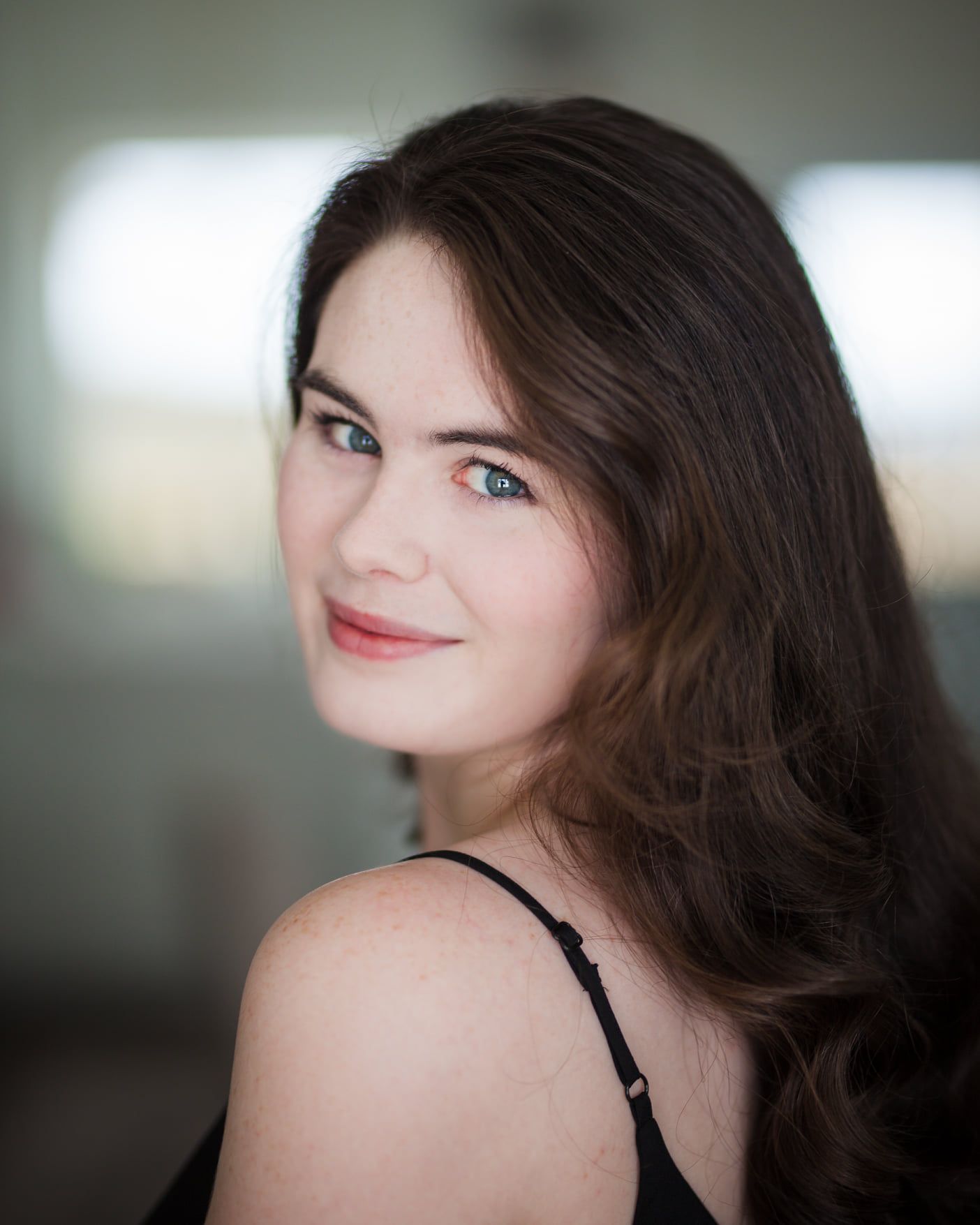 A portrait featuring soft lighting and natural makeup against a blurred background.