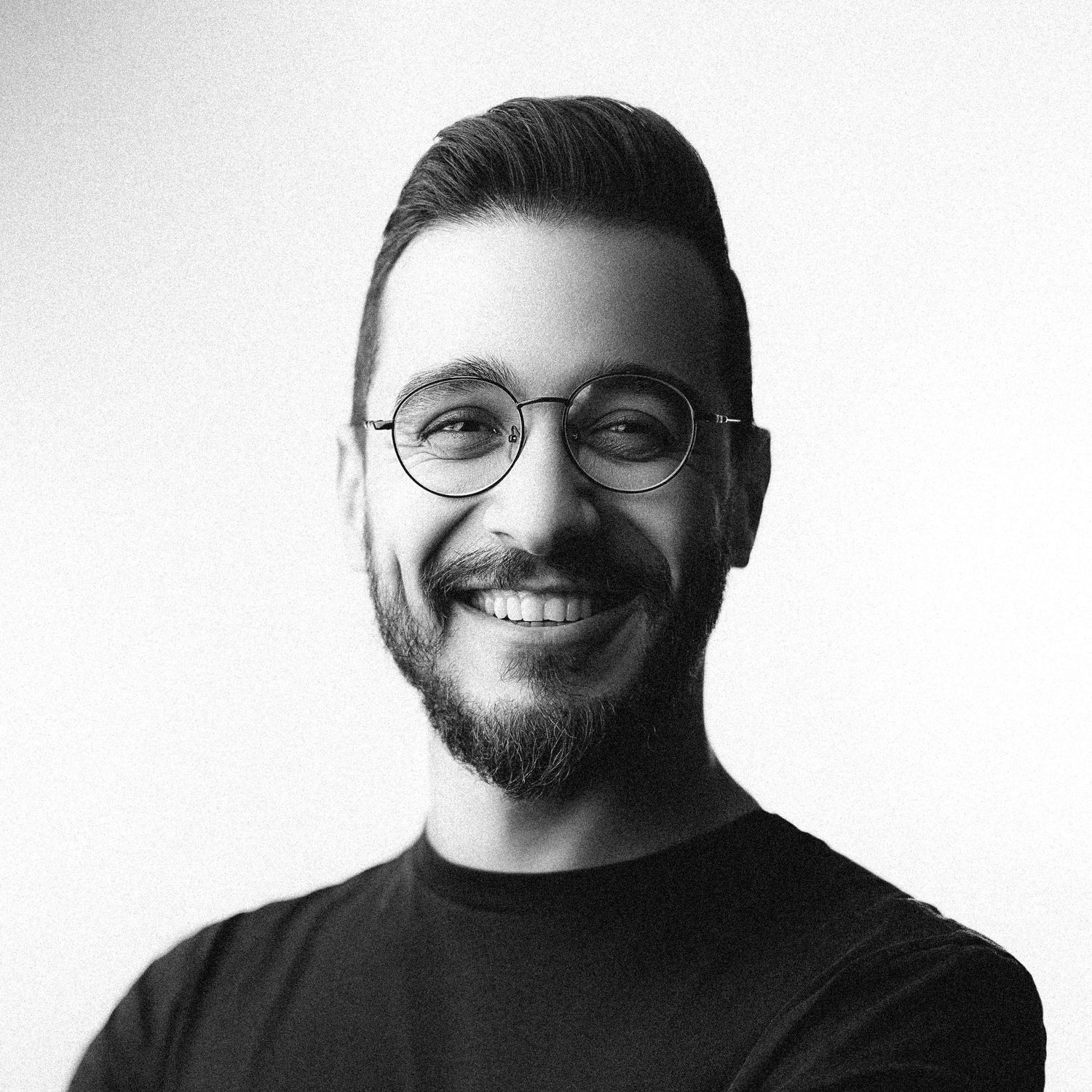 Black and white studio portrait of man in glasses and beard against white background.