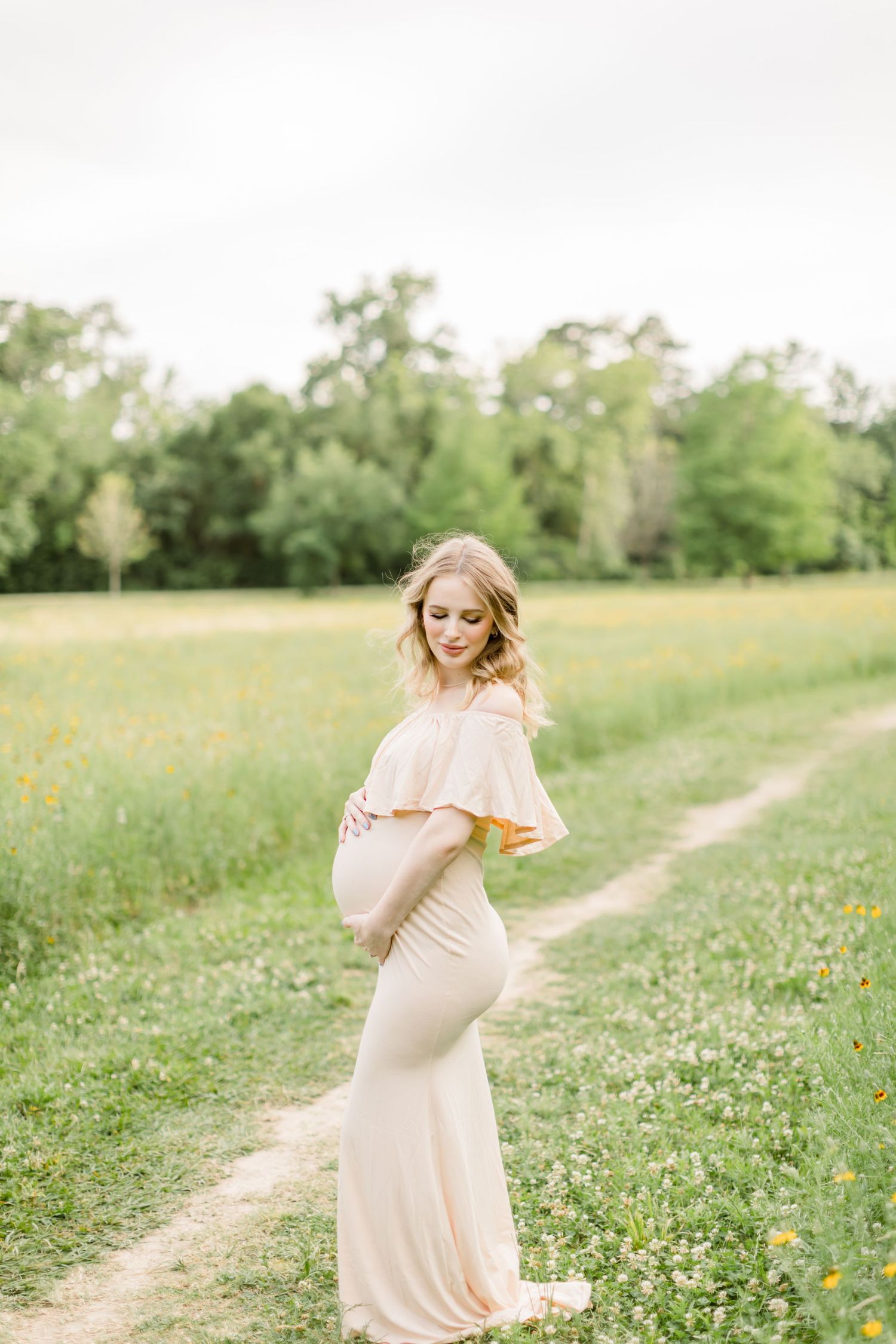 A dreamy maternity portrait along a winding path with wildflowers and soft lighting.