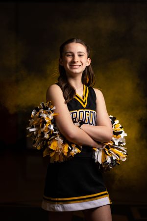 Cheerleader poses confidently with black and gold pom poms in Dragons uniform against dark backdrop.