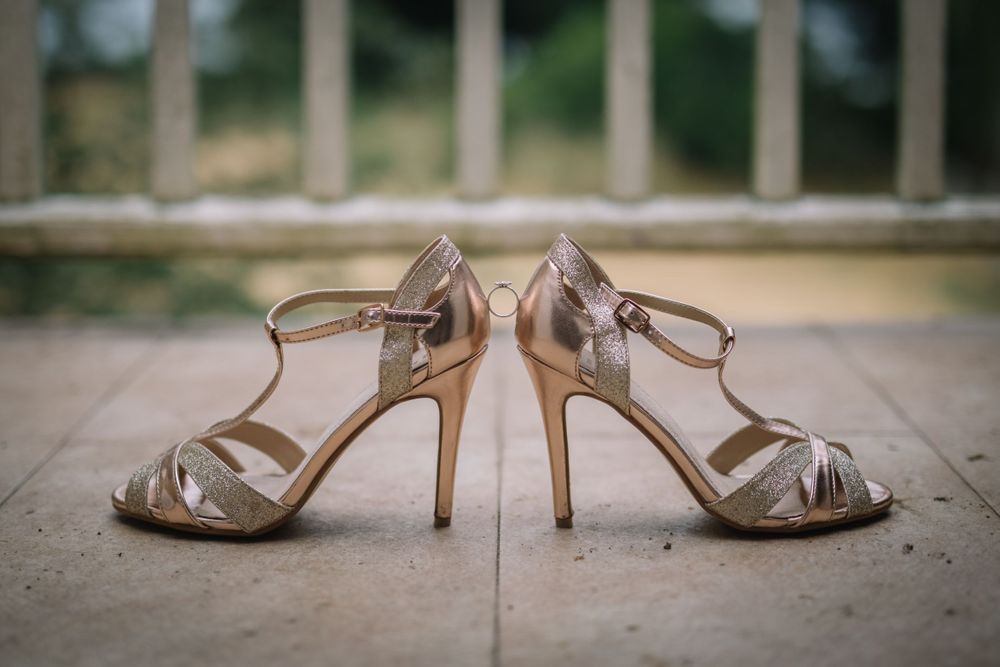 Elegant champagne-colored strappy wedding heels photographed on stone floor.