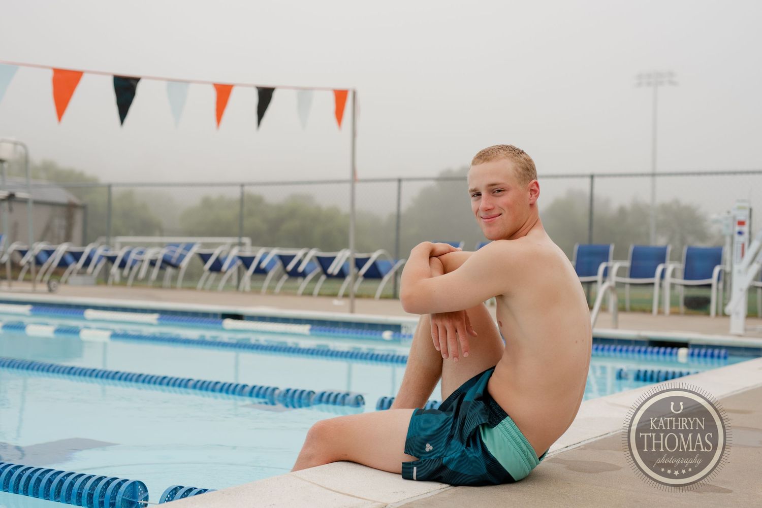A swimmer sits at the edge of an outdoor pool with blue lounge chairs and lane lines visible.
