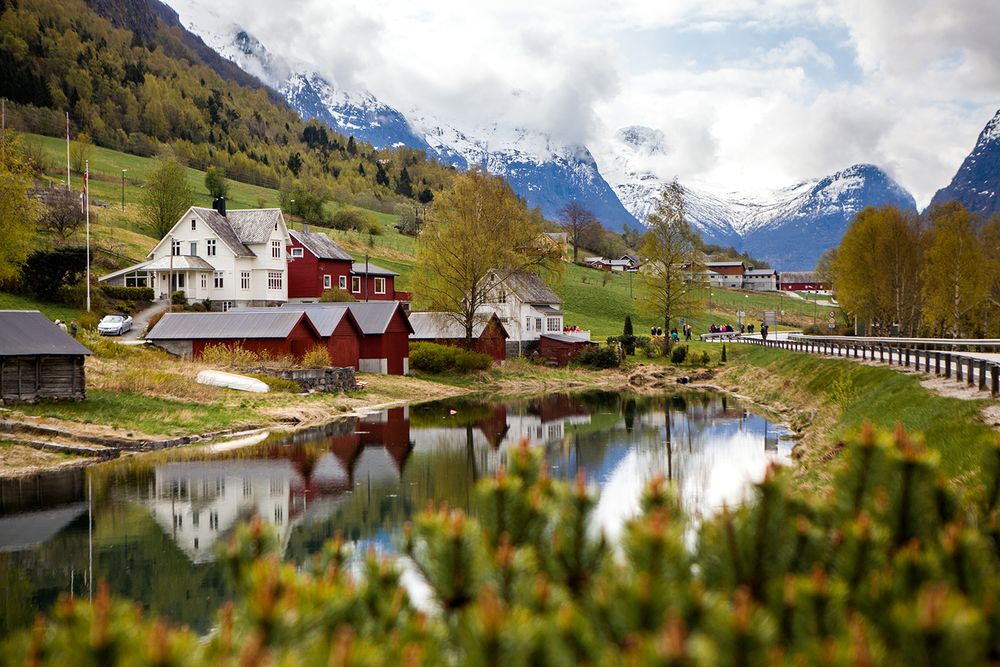 Picturesque Norwegian village nestled in valley with snow-capped mountains and reflective lake.