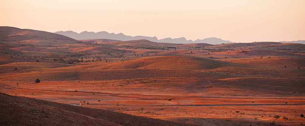 Rolling red desert hills stretch towards distant mountains at dusk.