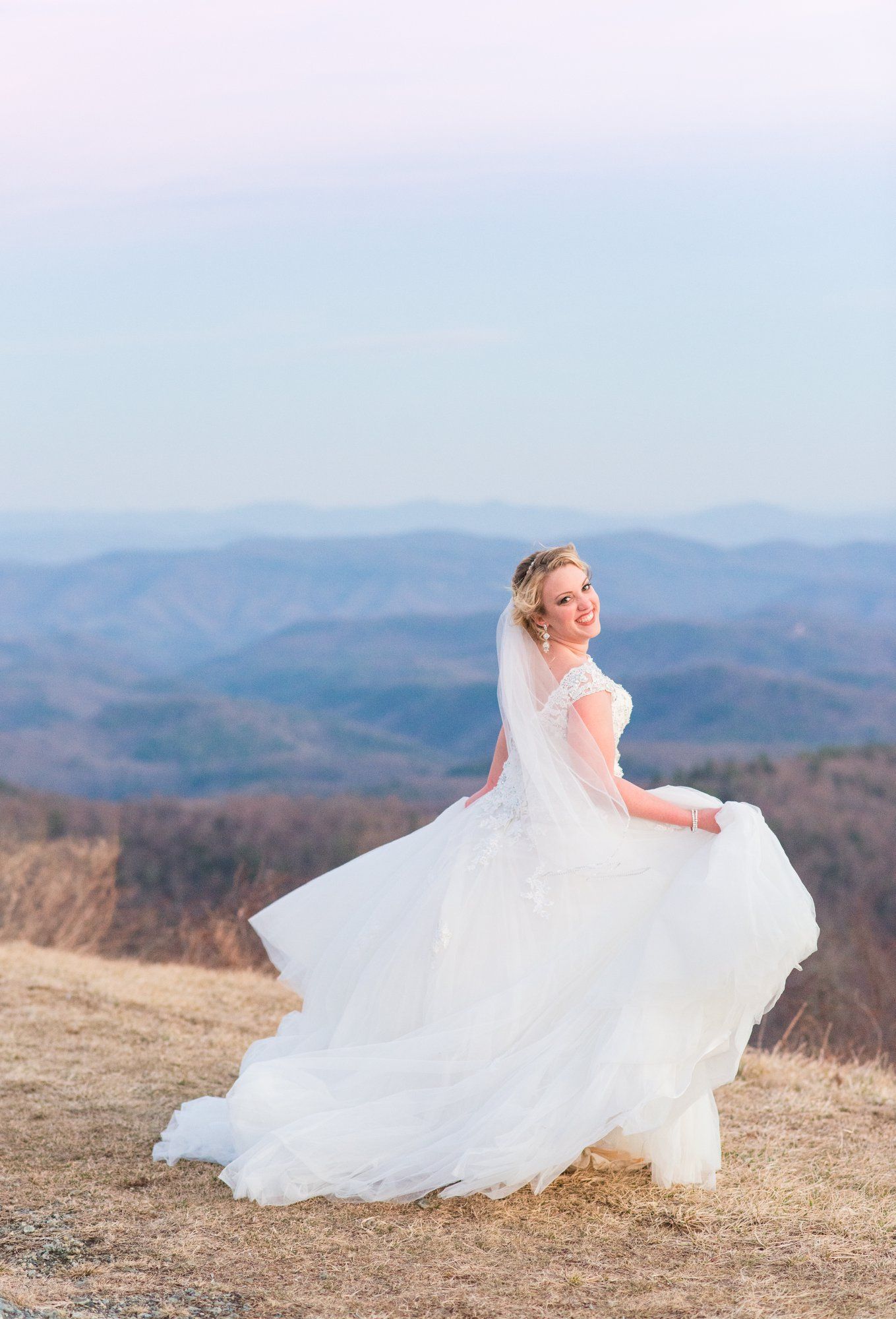 Flowing white wedding dress twirls against mountain landscape backdrop at sunset.