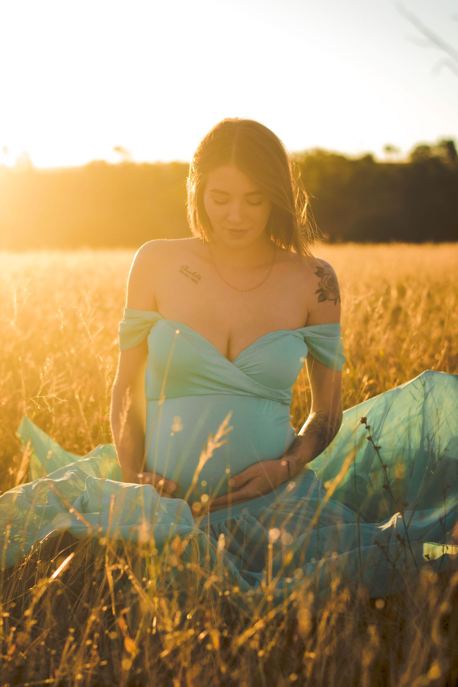 Person in light blue dress sitting in golden wheat field at sunset.