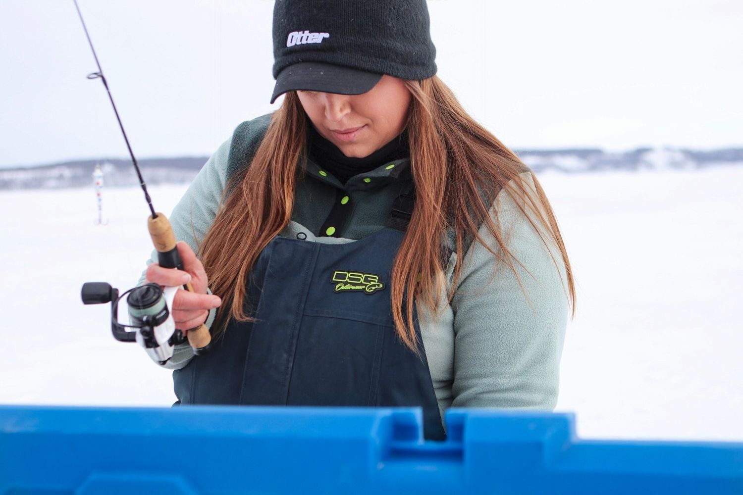 Ice angler using a white spinning reel while winter fishing on a frozen lake.