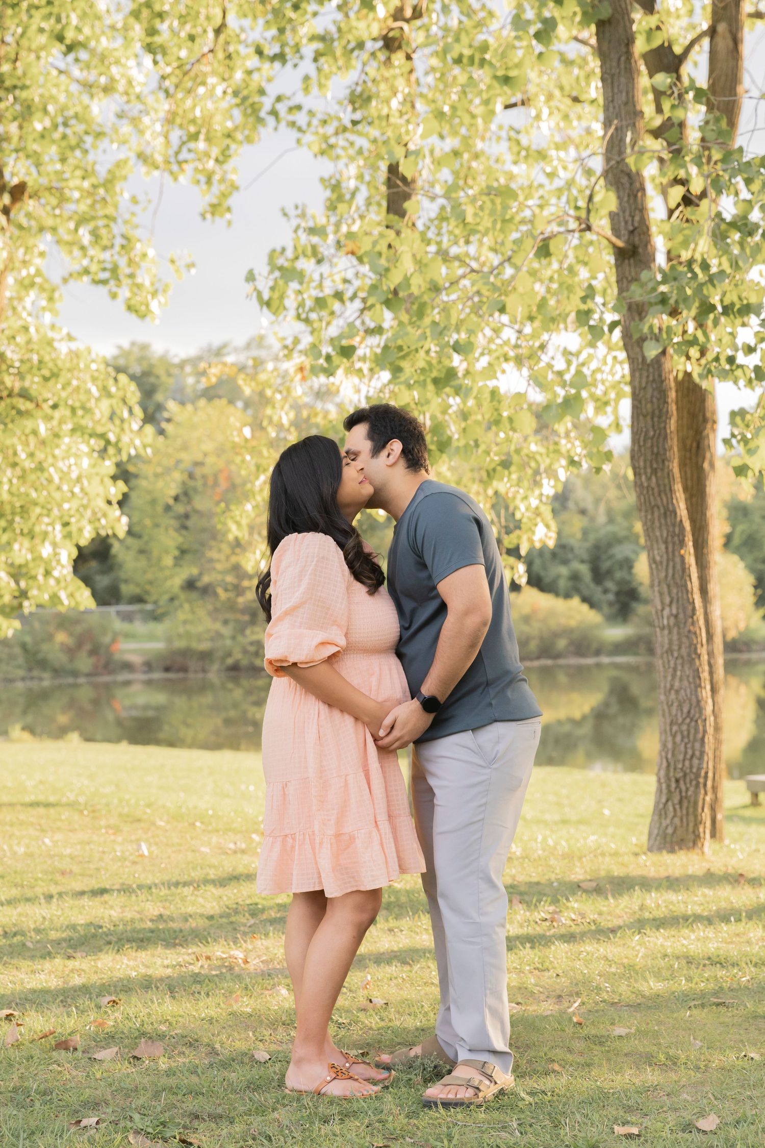 pregnant couple holding her belly as her husband gives her a kiss at sylvan glen lake park
