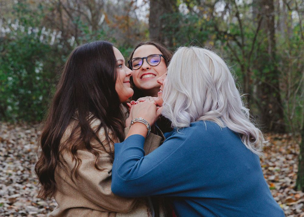 Three people sharing an affectionate moment outdoors during fall season.