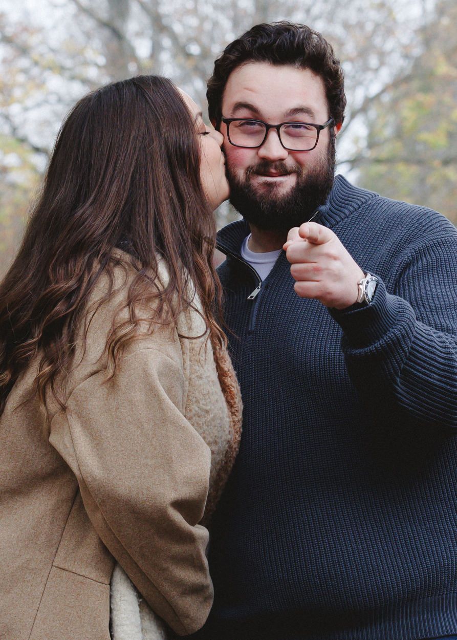 A couple shares an affectionate moment outdoors on a fall day.
