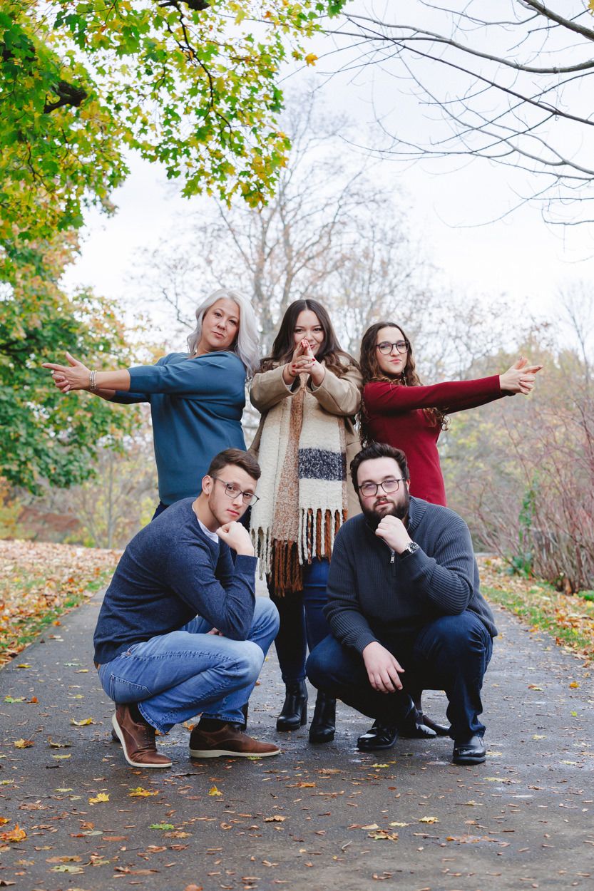 A group of five friends strike playful poses on a leaf-covered path during autumn.