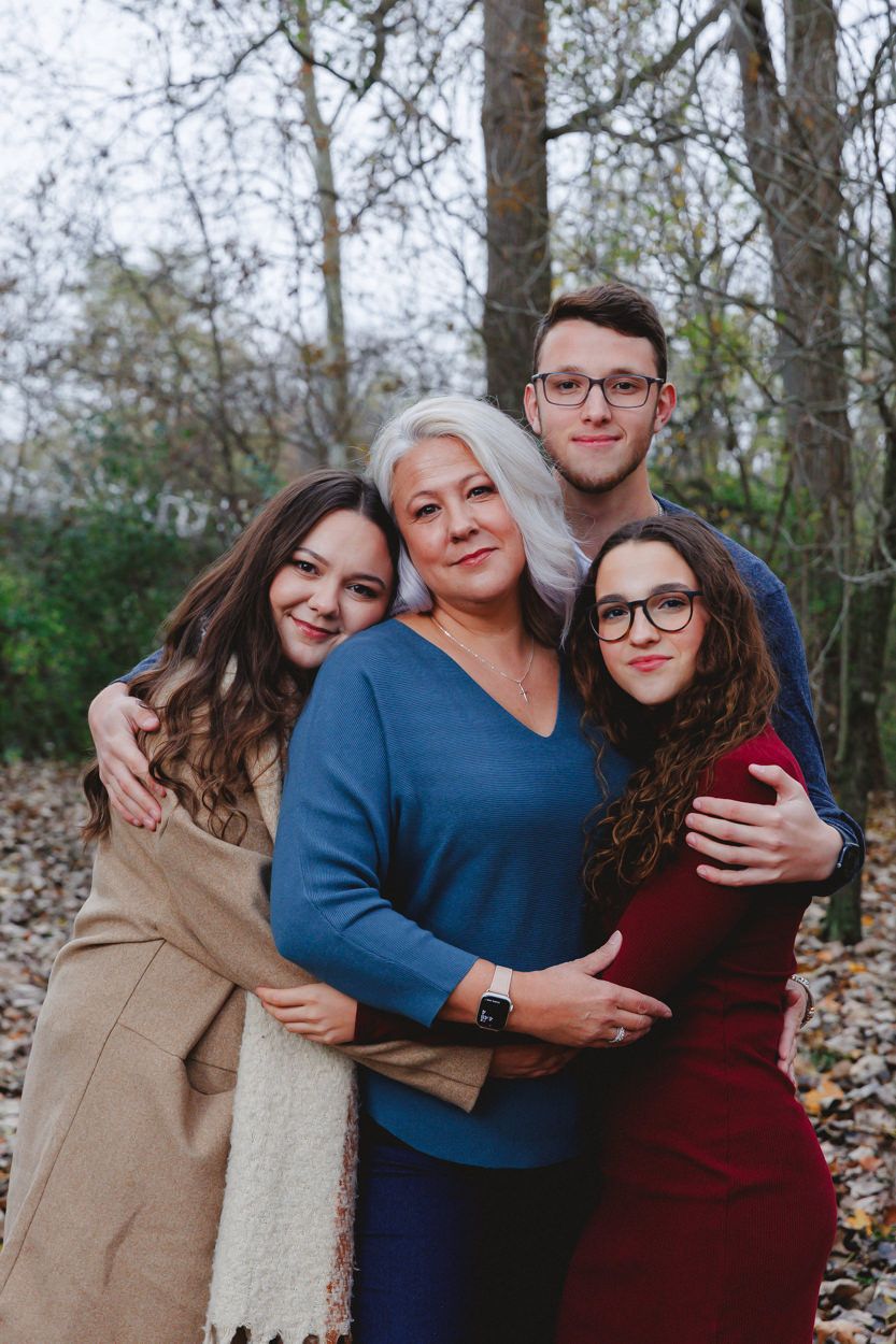 Family group portrait with coordinated outfits standing together in a wooded autumn setting.