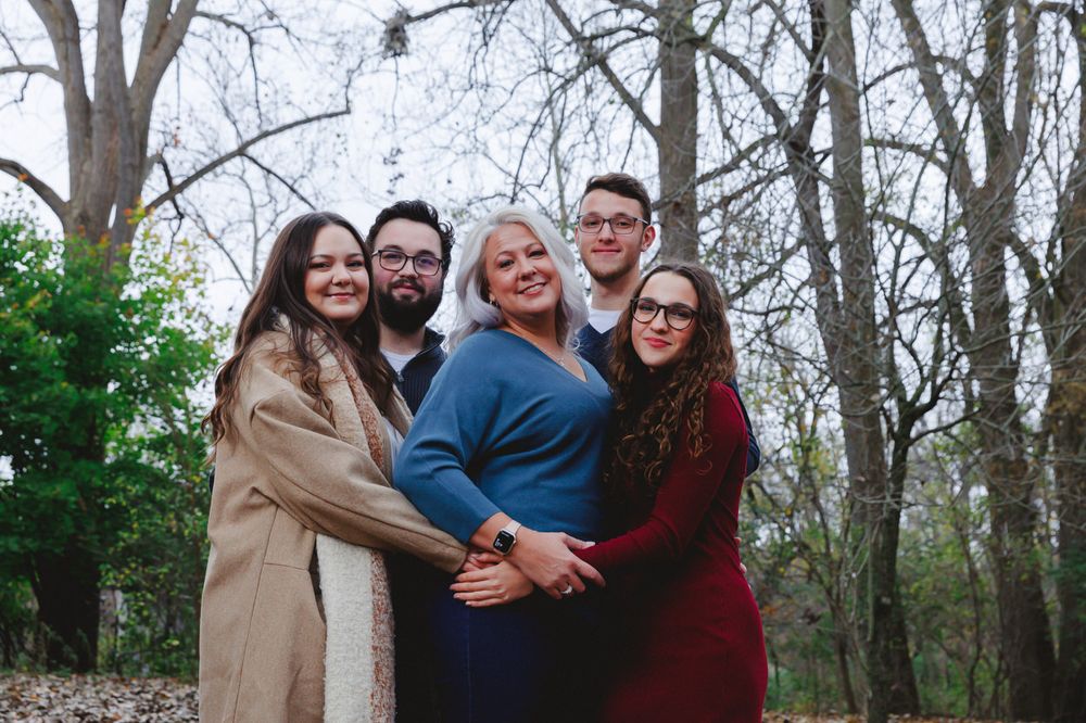 Group of people hugging and laughing together outdoors in casual fall attire.