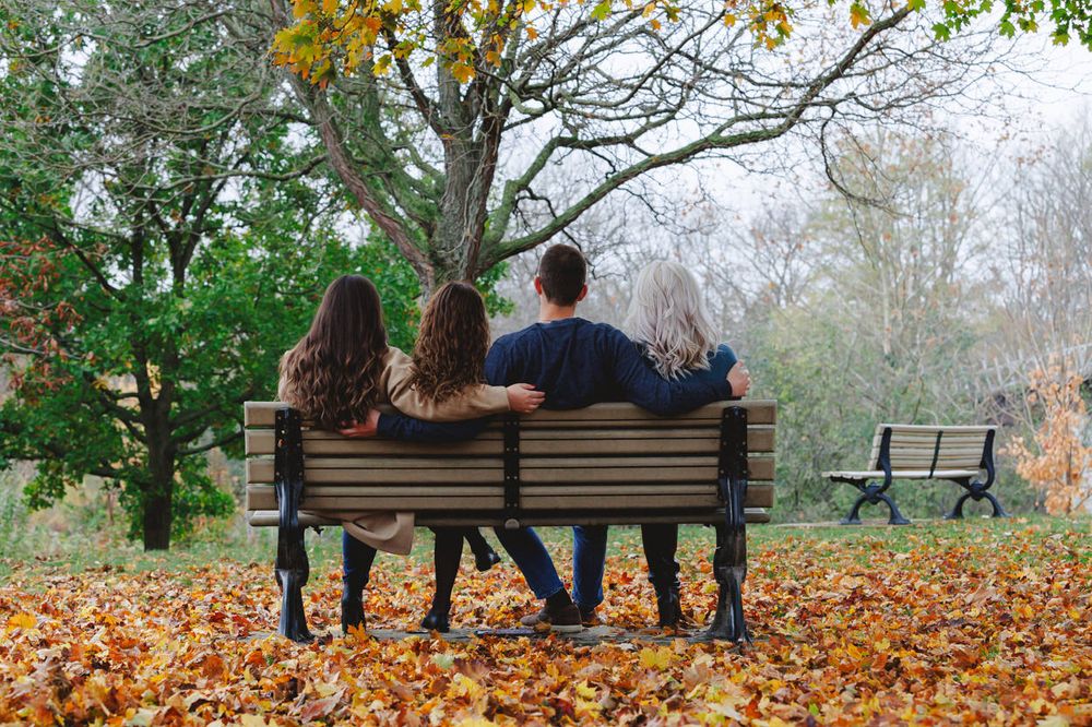 Back view of group sitting together on park bench surrounded by autumn foliage.