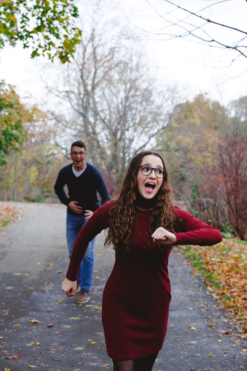 Playful autumn portrait on leaf-covered path with burgundy dress and casual attire.