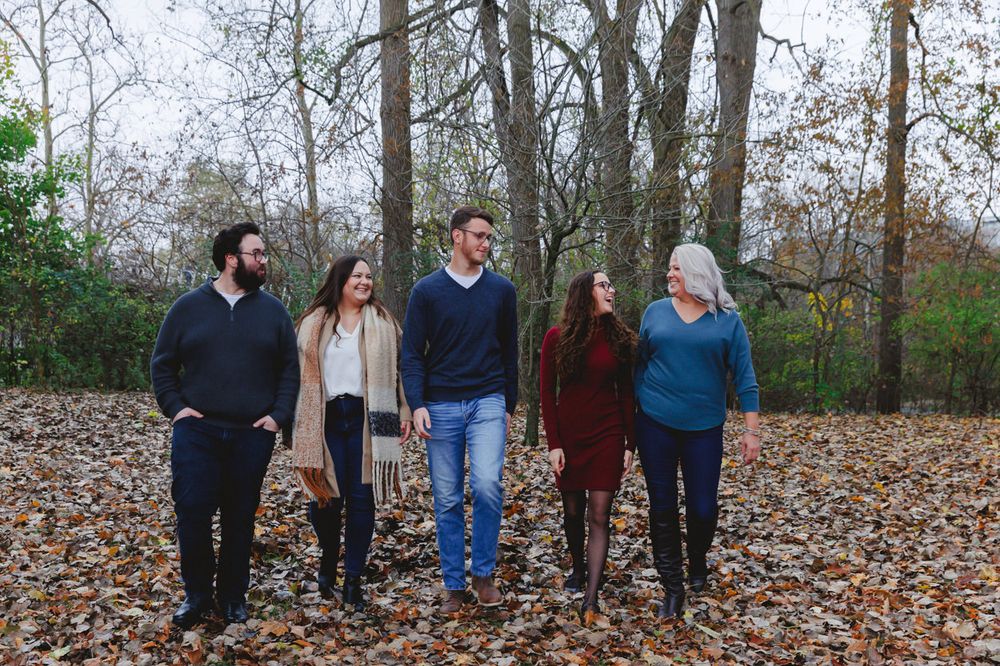 Group of five people walking together through fallen autumn leaves in a park setting.