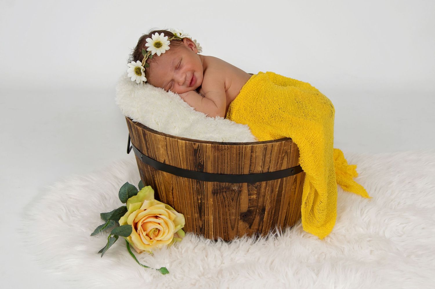newborn baby girl in bucket smiling with yellow headband and wrap