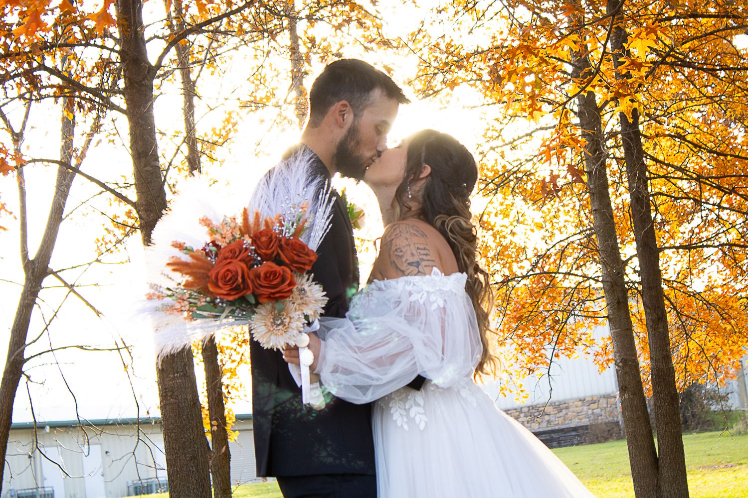 Autumn wedding photo with orange bouquet and fall foliage in background.
