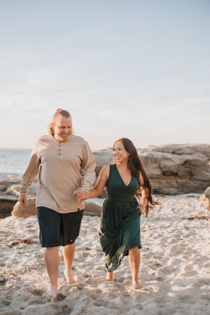 Couple running and laughing together on a sandy beach at sunset.