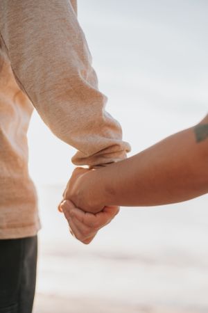 Close-up of intertwined hands against a soft beach backdrop.
