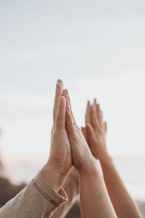 Two pairs of hands meeting in a high-five against a bright sky.